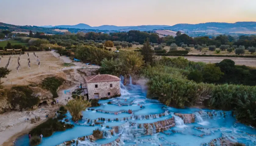 Cascate termali con acqua azzurra e un vecchio mulino, un'oasi di relax che ricorda le terme a Firenze.