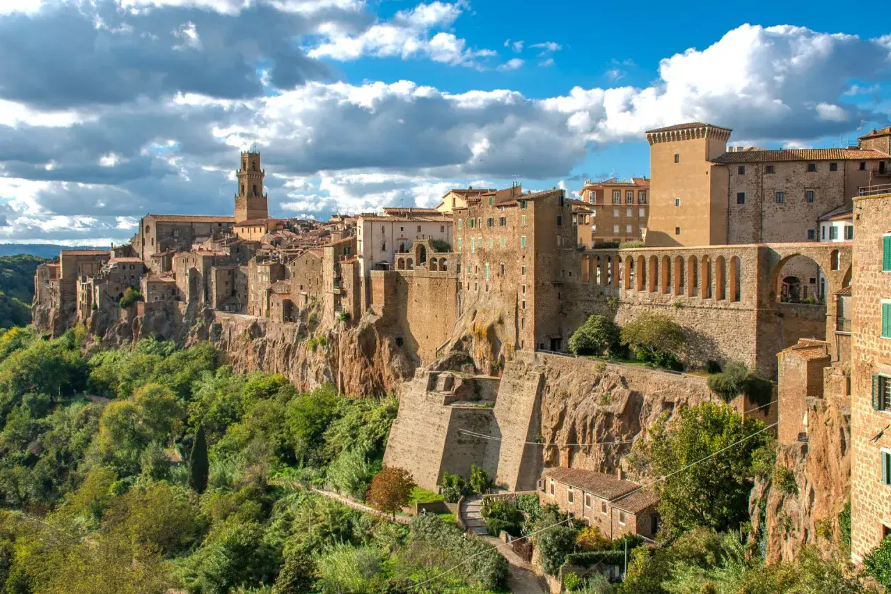 Un borgo arroccato su una rupe, con case in pietra e un campanile svettante, sembra una piccola Gerusalemme sotto un cielo azzurro e nuvoloso.