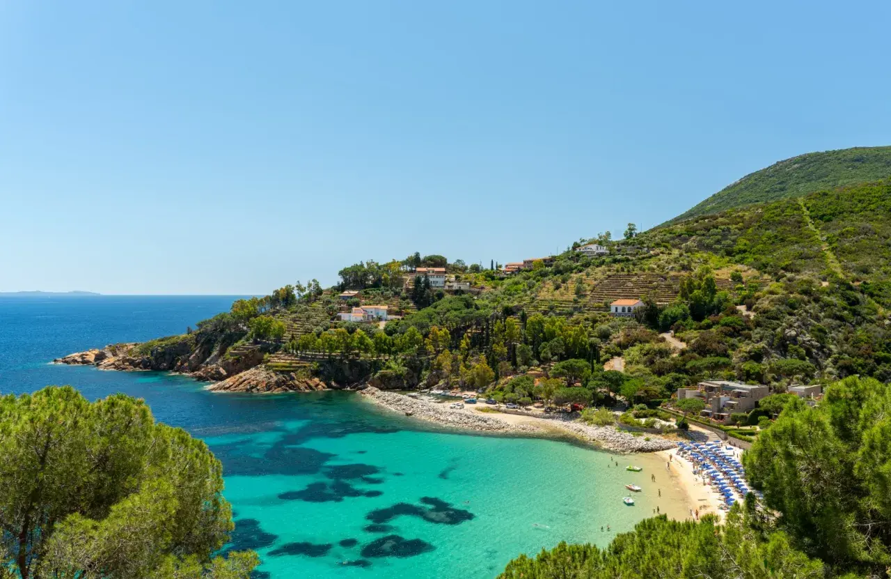 Incantevole baia con acque cristalline, spiagge dorate e case arroccate sulle colline verdi, un sogno di città toscane sul mare.