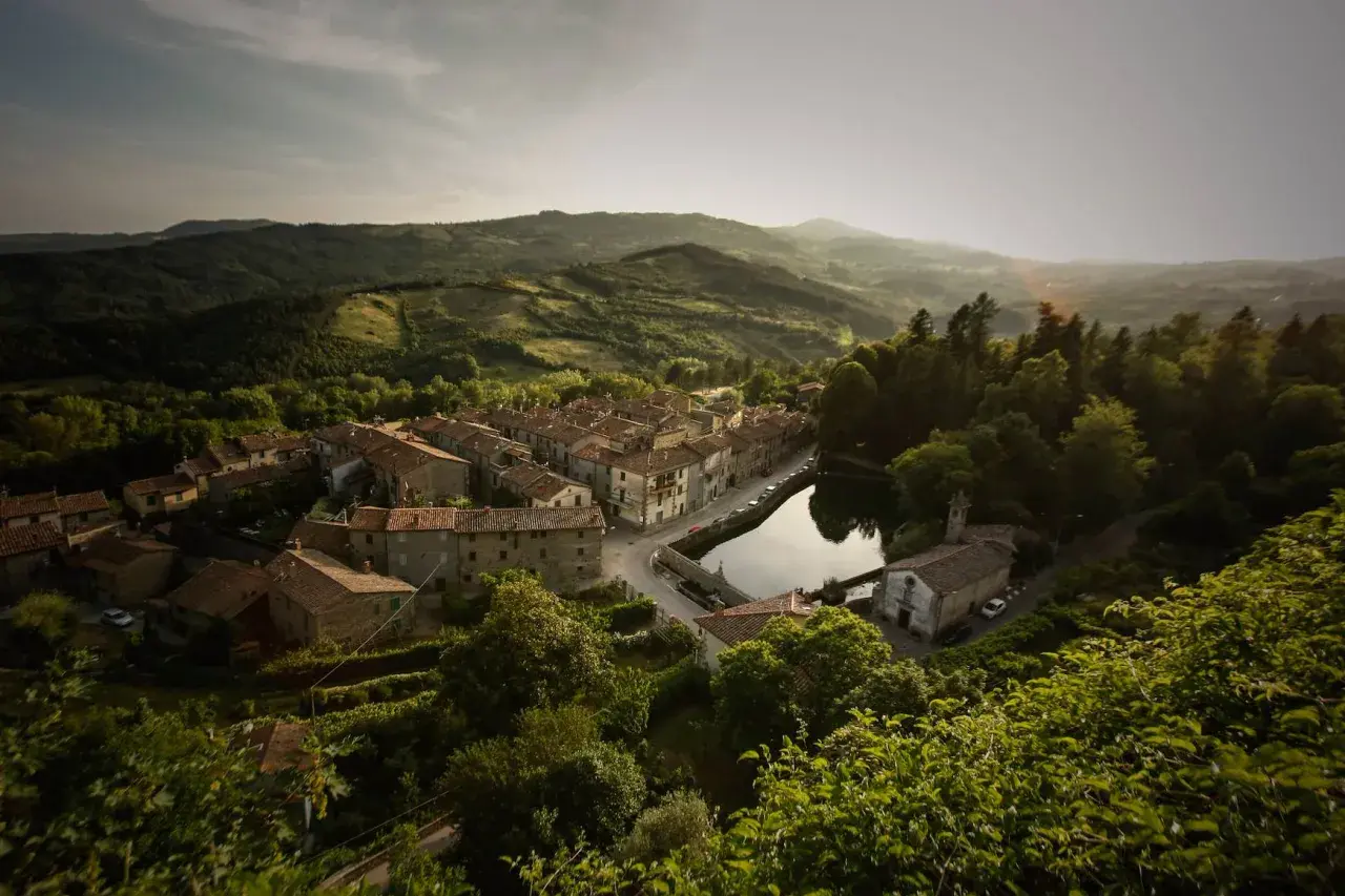 Peschiera Santa Fiora, un borgo toscano incastonato tra colline verdi, con case in pietra e un laghetto che riflette il cielo.