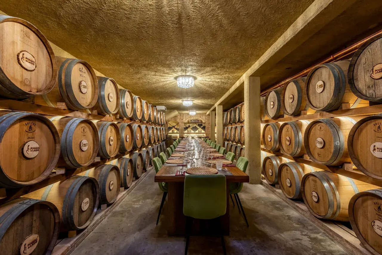 Un'elegante sala per una visita in cantina con degustazione, con botti di legno disposte su entrambi i lati e un lungo tavolo apparecchiato.