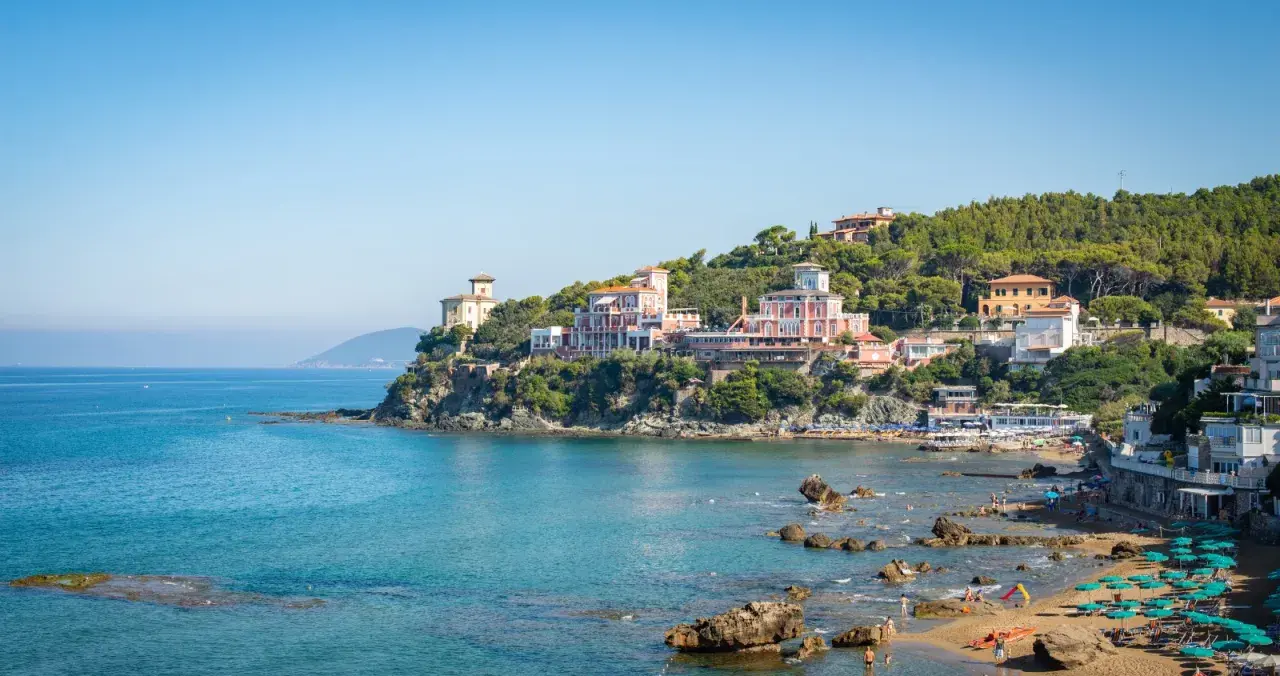Panorami mozzafiato di Castiglioncello, Italia, con ville storiche affacciate sul mare turchese e una spiaggia animata.
