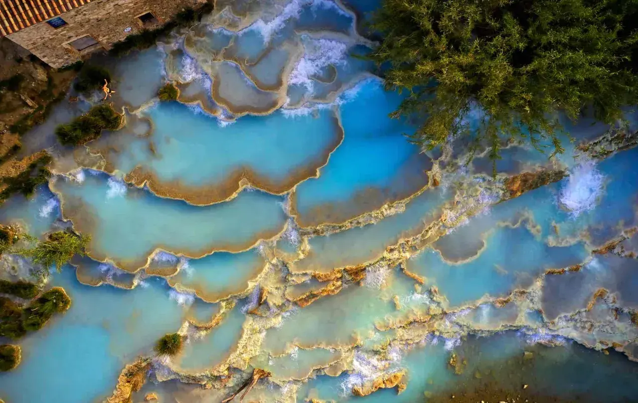 Cascate naturali di acqua turchese in un thermal spa Tuscany, con una persona che si rilassa tra le rocce calcaree.