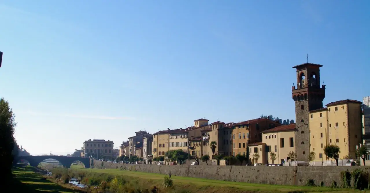 Edifici storici e una torre medievale si affacciano sul fiume nel pescia centro storico, sotto un cielo azzurro.