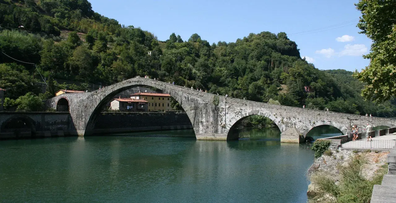 Il Ponte del Diavolo, con i suoi archi in pietra, attraversa un fiume verdeggiante, circondato da colline boscose.