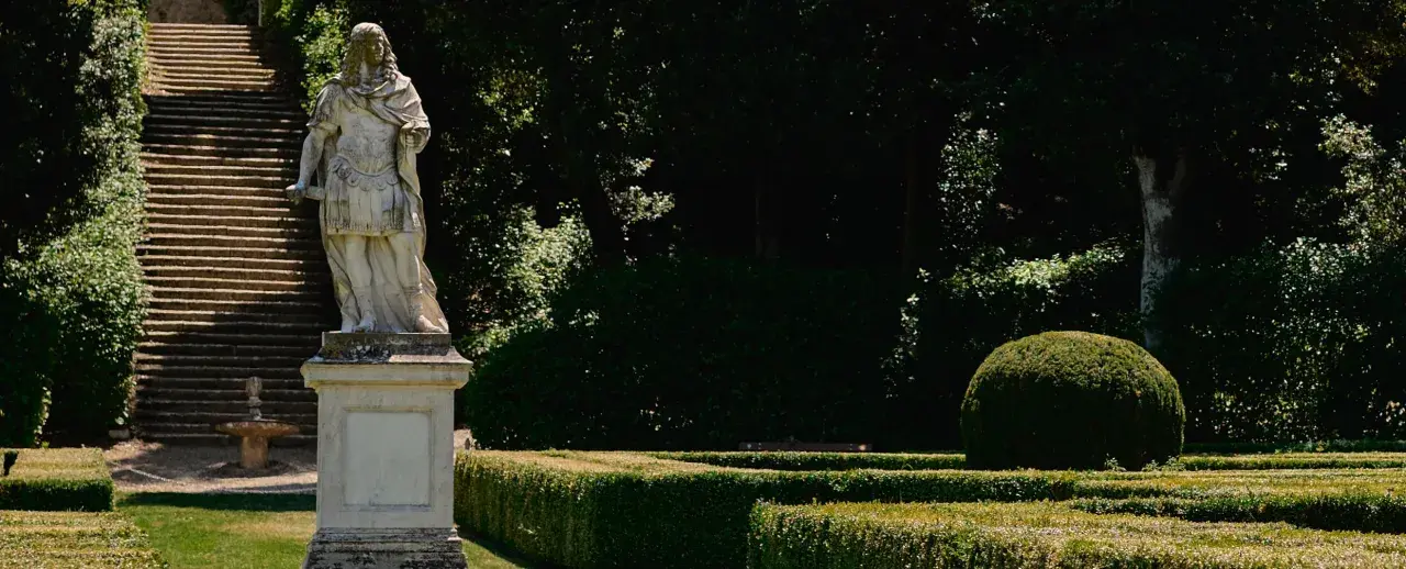 Statua romana domina una scalinata nei **Horti Leonini**. Giardini curati e alberi ombrosi creano un'atmosfera serena.