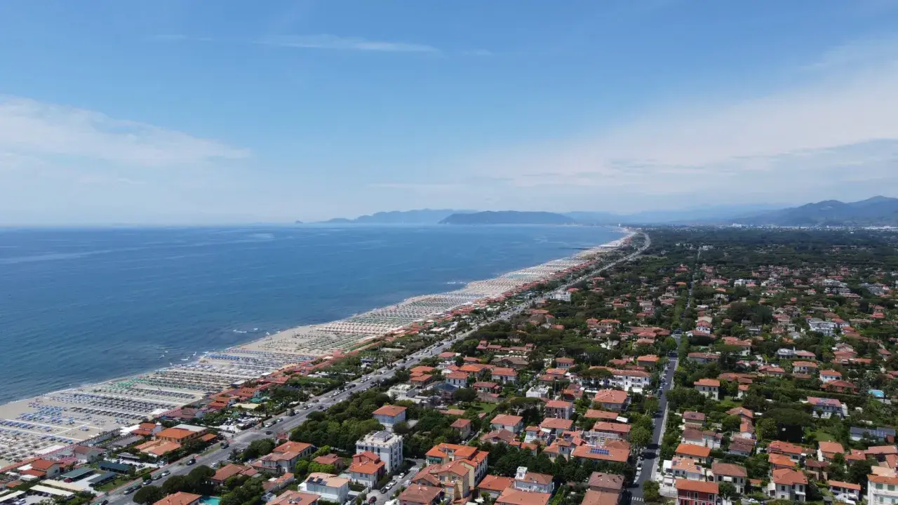 Vista aerea della costa toscana, dove si trova Forte dei Marmi, con spiagge attrezzate, mare blu e un fitto tessuto urbano.