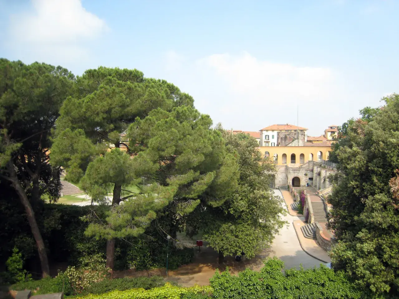 Un angolo del giardino Scotto, con pini marittimi e un edificio storico con arcate.