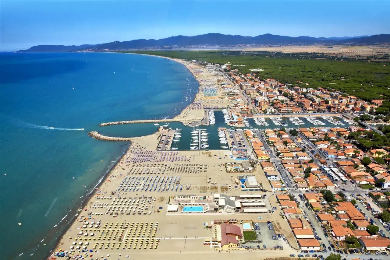 Vista aerea di Marina di Grosseto con spiaggia affollata, porto turistico pieno di barche e case con tetti rossi.