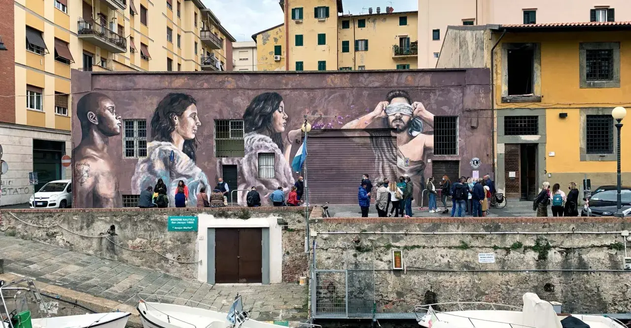 Un imponente murales livornese raffigura tre volti, uno bendato, con persone che osservano l'opera d'arte.