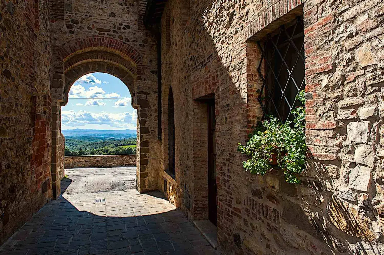Un vicolo in pietra a San Gusmè, con un arco che rivela un paesaggio collinare toscano.