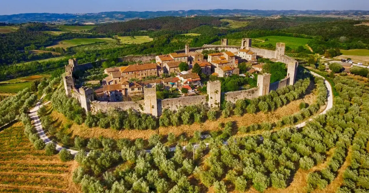 Il centro storico di Monteriggioni, un borgo medievale fortificato, si erge su una collina circondato da mura e torri, immerso nel verde della campagna toscana.