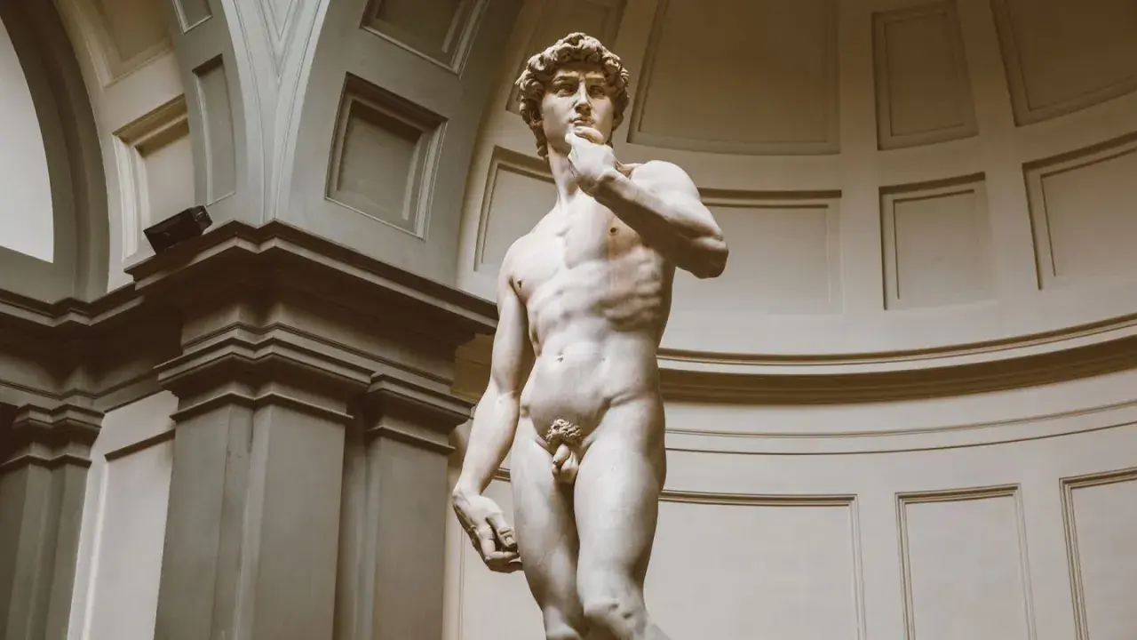 Michelangelo's David statue, a marble sculpture of a nude male figure, stands in a grand hall.