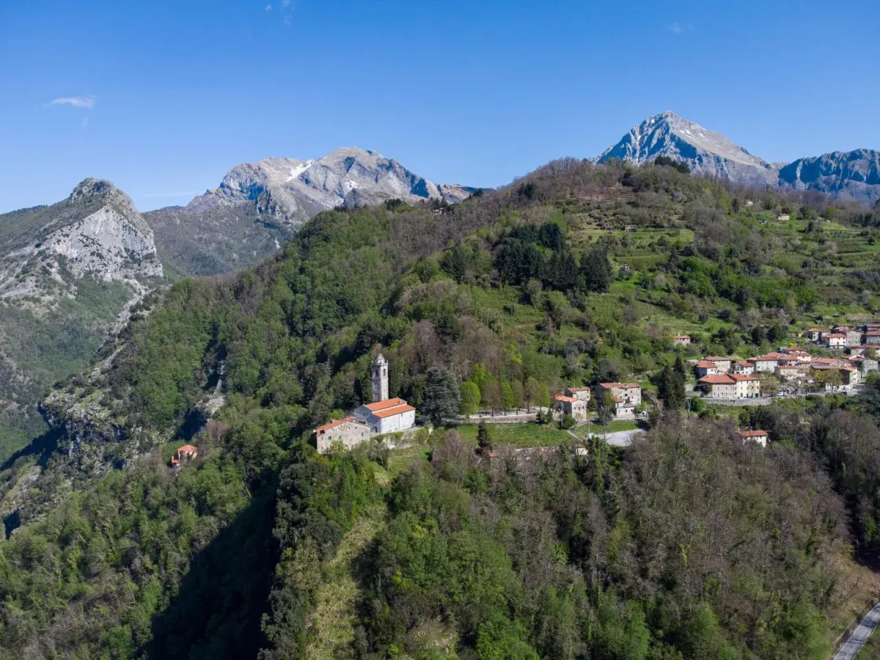 Sant'Anna di Stazzema: un borgo tra monti verdi e cielo azzurro. La chiesa domina il paesaggio, un luogo da scoprire.