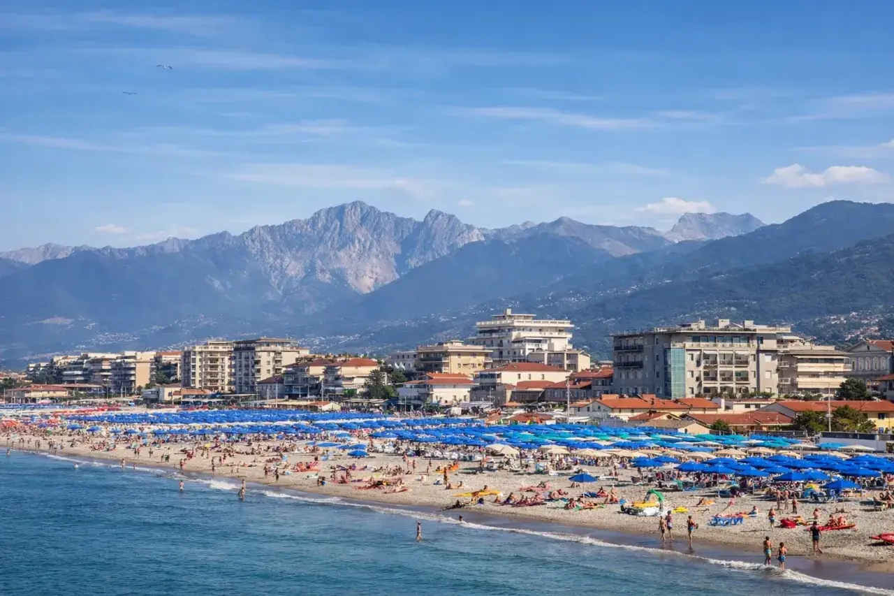 Una vivace spiaggia libera al Lido di Camaiore, con montagne imponenti sullo sfondo e un mare azzurro.