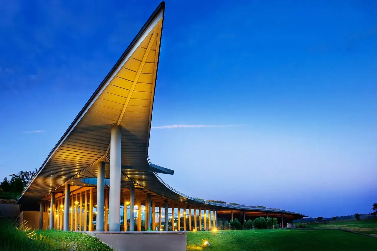 La tenuta ammiraglia Frescobaldi, con la sua architettura moderna illuminata, si staglia contro il cielo serale. Le recensioni lodano questo luogo.