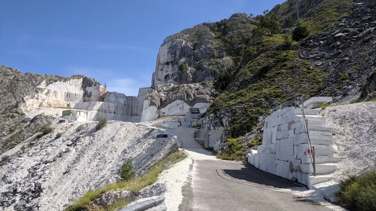 Un imponente passo del vestito di marmo bianco si erge su un fianco della montagna, con blocchi grezzi e una scala scavata nella roccia.