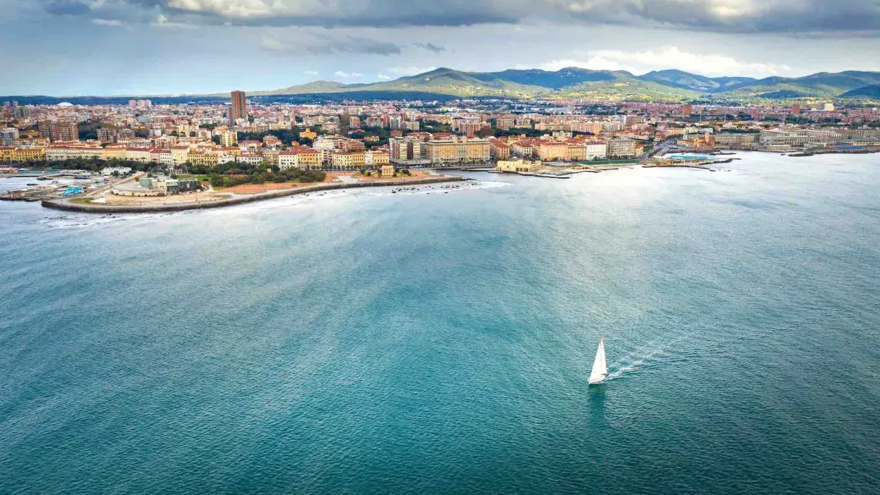 Un veliero solca il mare di Livorno, con la città e le colline sullo sfondo.