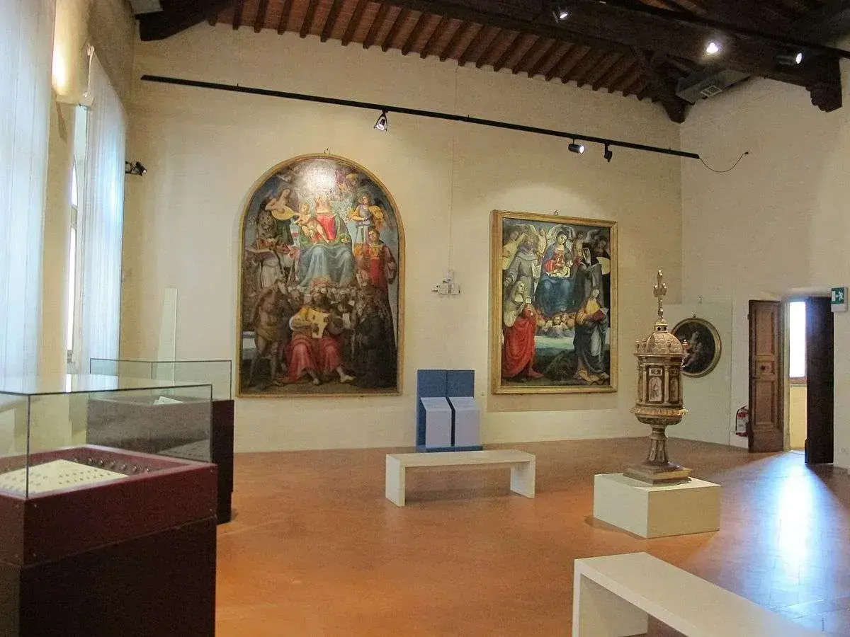 Interno di una sala dei musei di Arezzo con dipinti rinascimentali, un'urna e teche espositive.