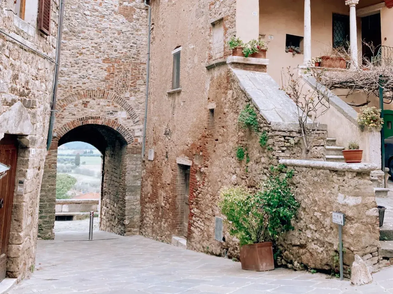 Antico vicolo con arco in pietra, tipico dei borghi vicino Rapolano Terme. Scale in pietra e piante in vaso aggiungono fascino.