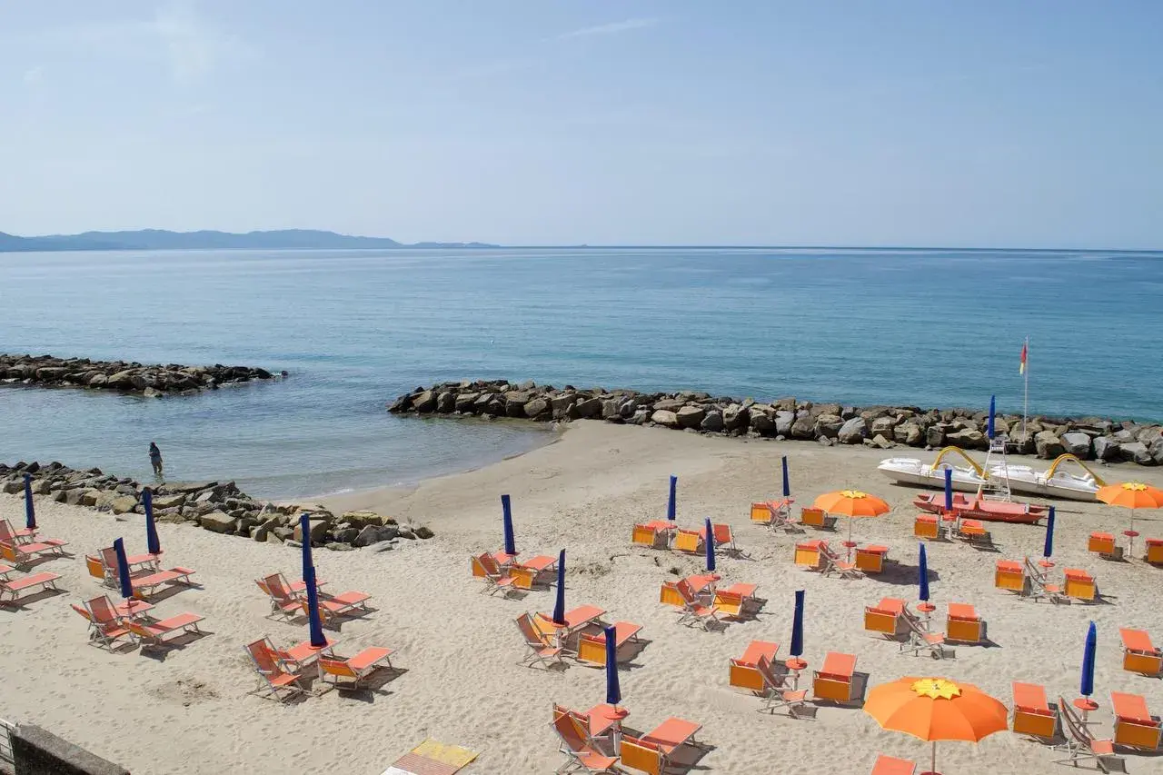 Spiaggia attrezzata con lettini e ombrelloni arancioni, mare azzurro e scogli. Un sogno di vacanza a Pratoranieri Follonica.