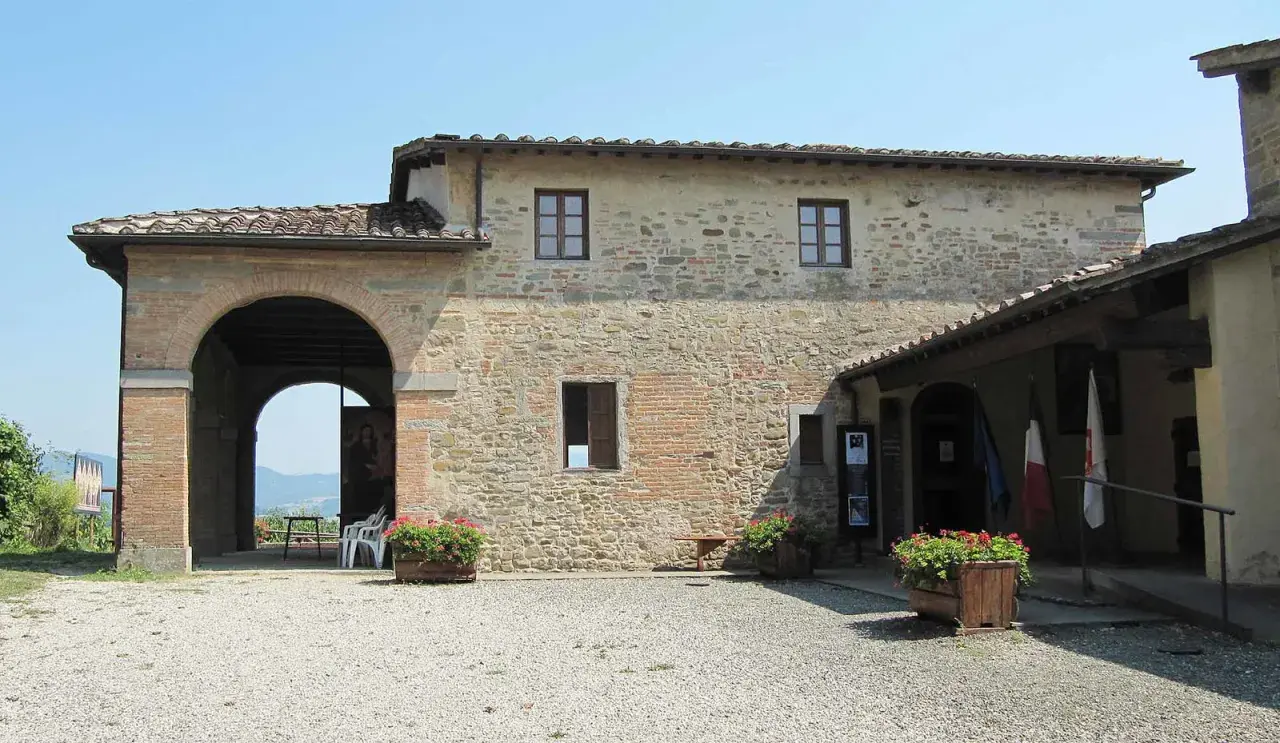 La casa di Giotto, un edificio in pietra con un grande arco, fiori rossi e bandiere.