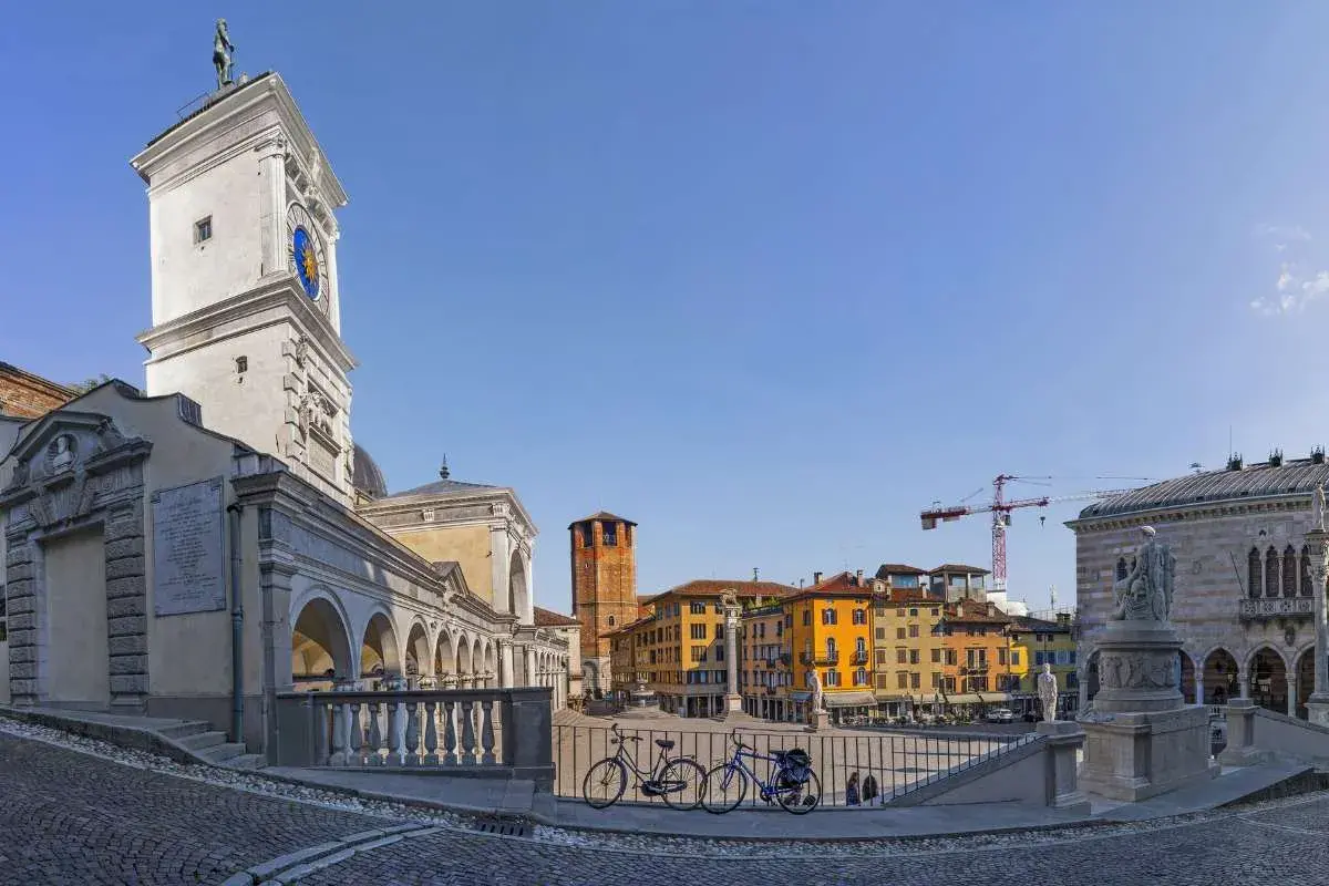 La piazza della Libertà, con la sua torre dell'orologio, edifici colorati e due biciclette in primo piano, sotto un cielo azzurro.
