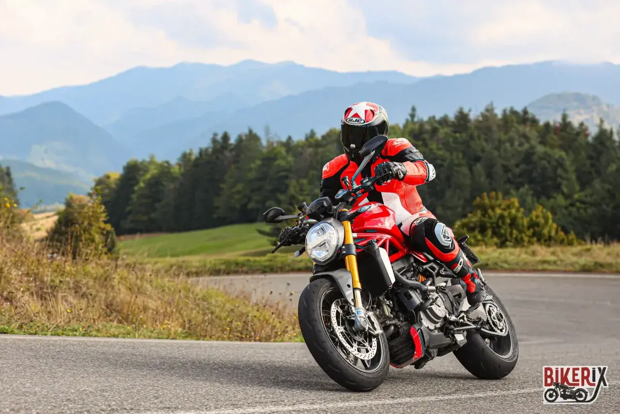 Motociclista in tuta rossa affronta una curva sul passo del giogo, con montagne sullo sfondo.