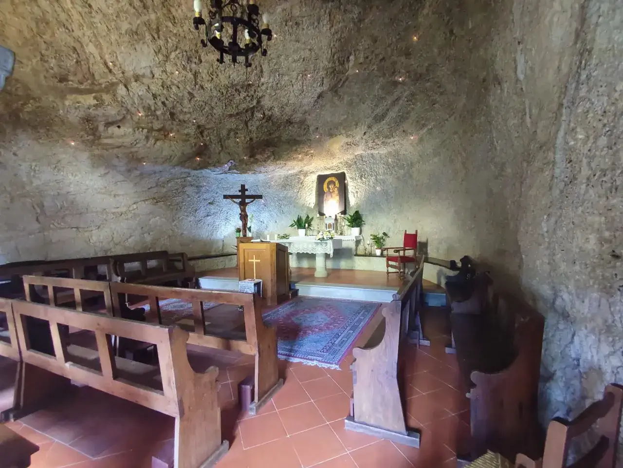 Interno dell'eremo di Calomini, con panche in legno, altare, crocifisso e un'icona sacra incastonati nella roccia.