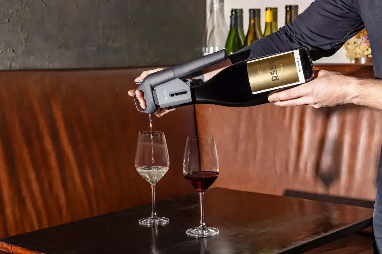 Versando vino bianco da una bottiglia con un erogatore Coravin, accanto a un bicchiere di vino rosso. Un tipo di vino da scoprire.