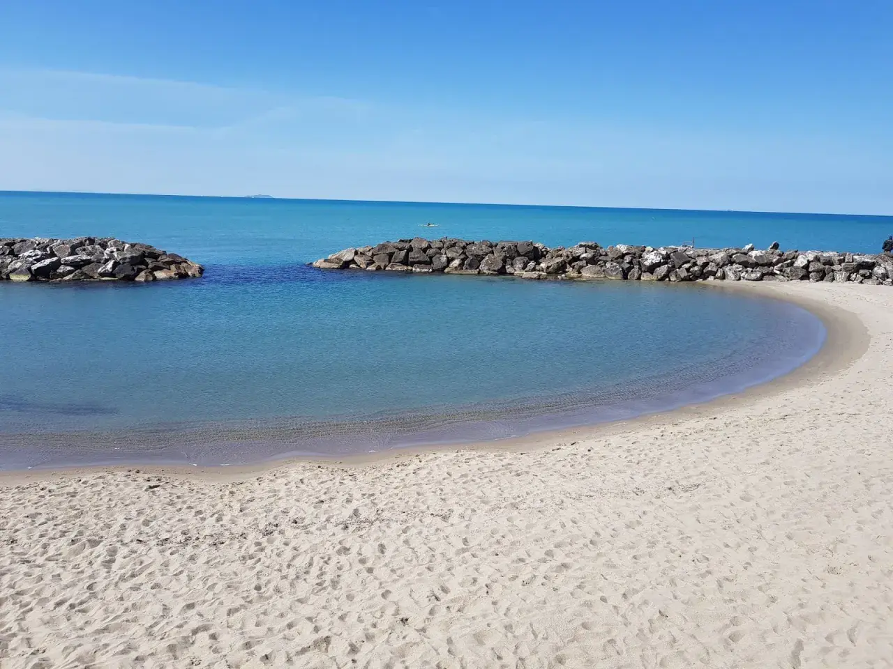 Spiaggia di Marina di Pisa con acque calme e dighe frangiflutti in pietra.