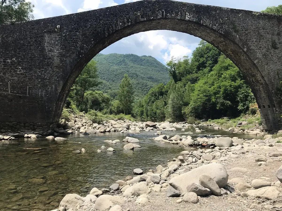 Il ponte di Castruccio, con il suo arco maestoso, sovrasta un fiume serpeggiante tra rocce e vegetazione lussureggiante.