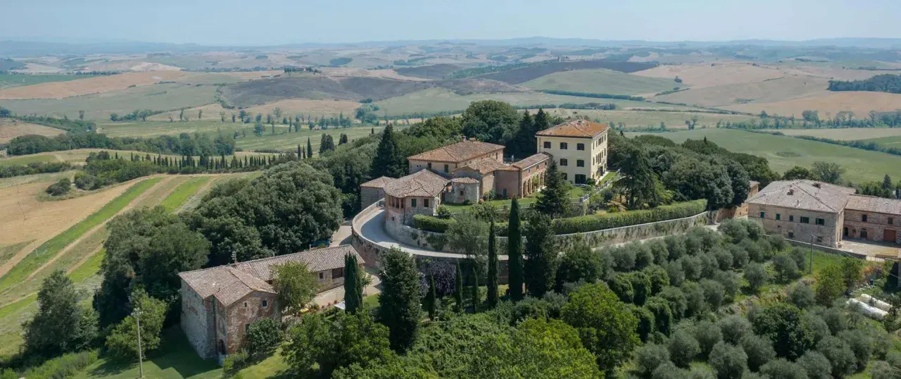 Un borgo toscano con casali in pietra e un edificio giallo, immerso nel verde e con dolci colline sullo sfondo. Castelnuovo Tancredi, un'oasi di pace.