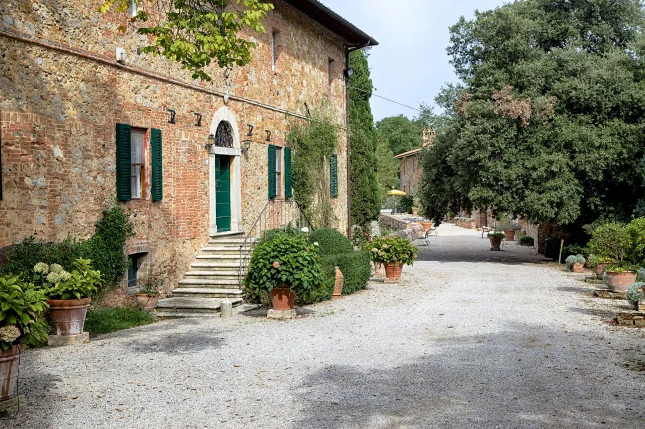 Ingresso della fattoria del colle Trequanda, con scalinata in pietra, porta verde e piante in vaso.