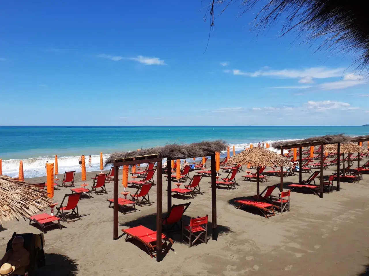Marina di Bibbona spiagge più belle: lettini rossi e ombrelloni di paglia sotto un cielo azzurro, con il mare calmo all'orizzonte.