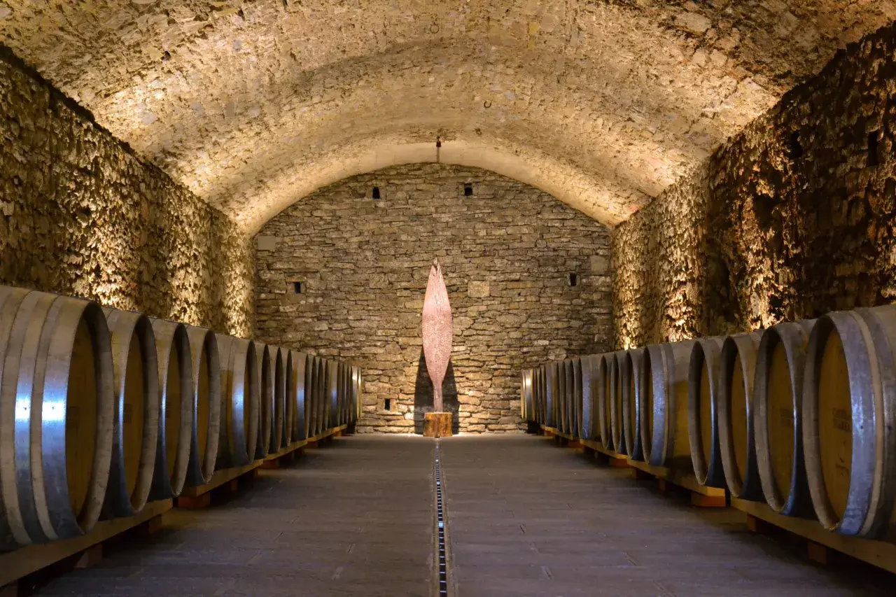 Cantine in pietra con botti di legno, un'installazione artistica al centro. Perfetto per una visita cantine Chianti.