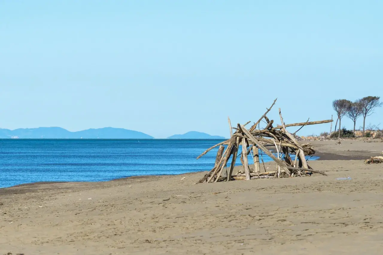 Spiaggia del Parco dell'Uccellina con un rifugio di legni sulla sabbia e il mare blu all'orizzonte.