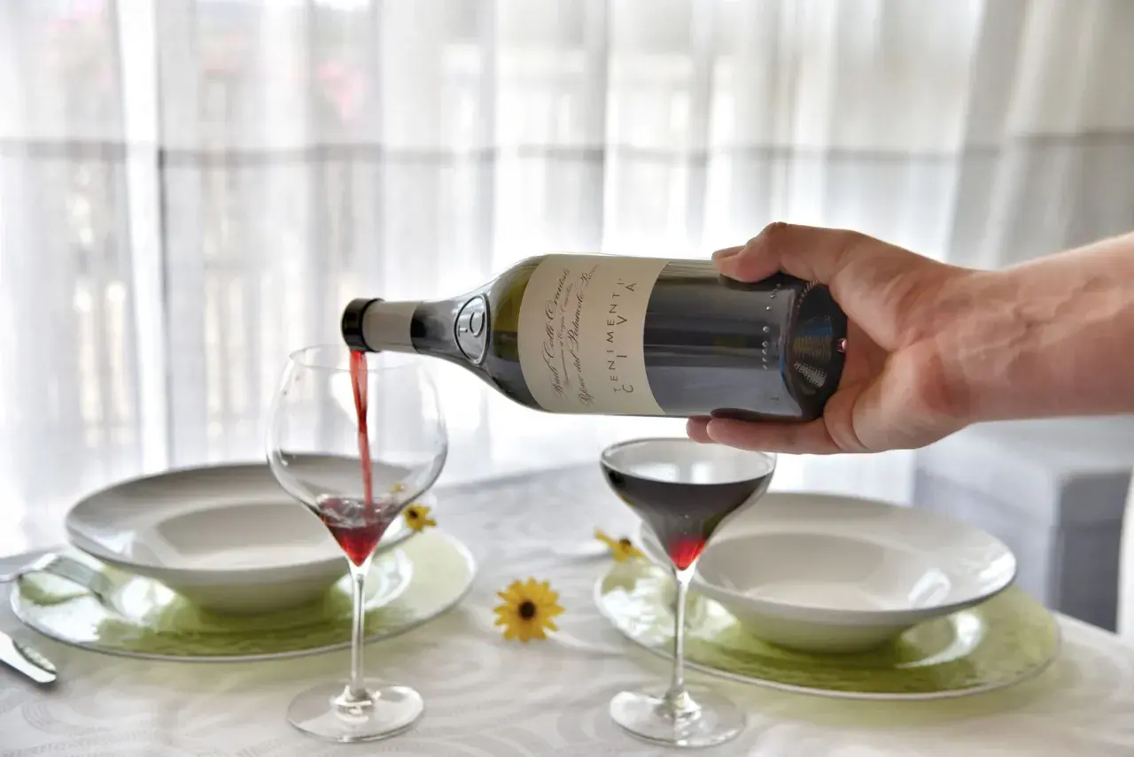 Versare vino rosso in un calice, un passo fondamentale per capire come si fa il vino rosso. La tavola è apparecchiata.