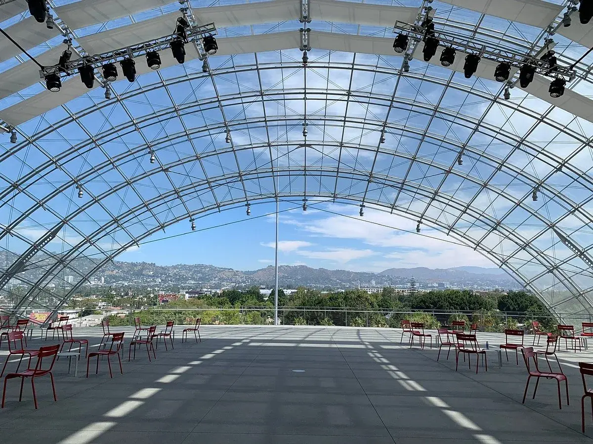 Spazi all'aperto del museo de la academia, con sedie rosse disposte e vista sulle colline di Los Angeles sotto una struttura a volta in vetro.