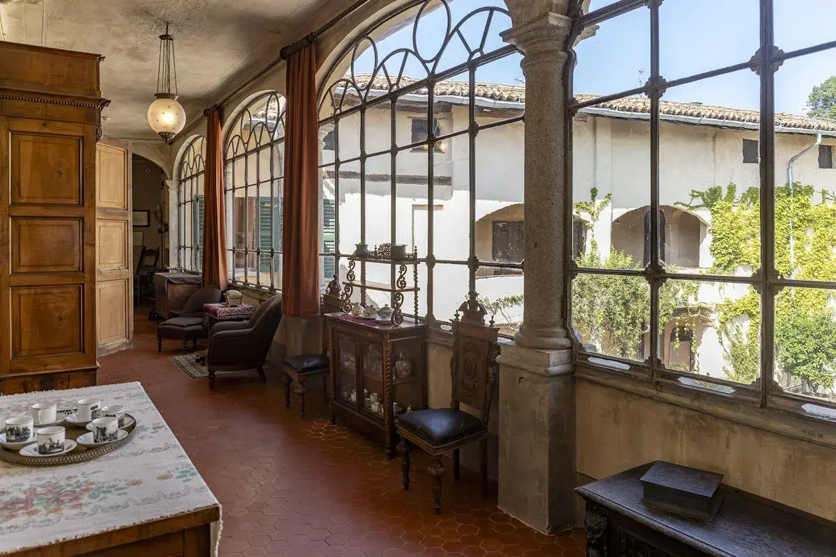 Interno elegante della villa Macchi con mobili d'epoca, grandi finestre ad arco e vista sul cortile verdeggiante.