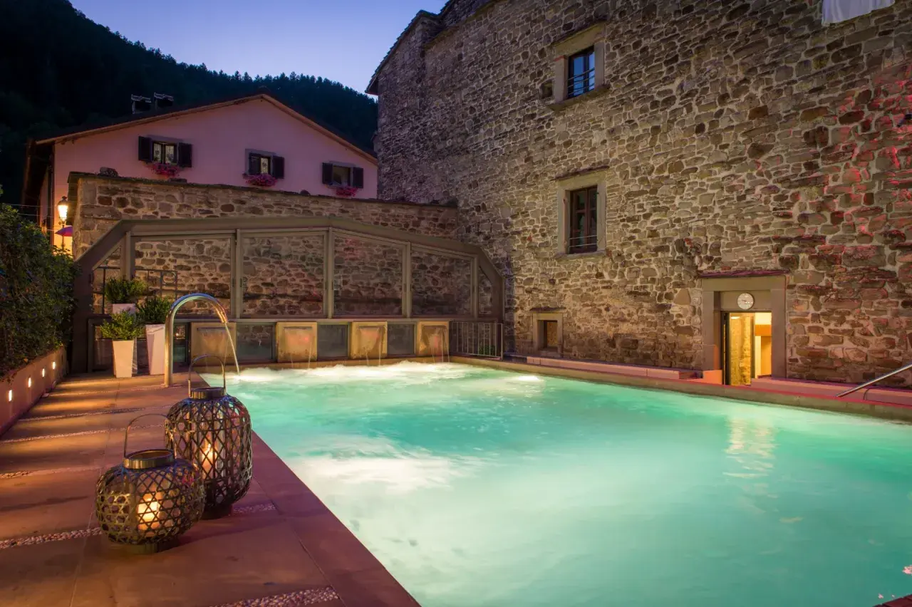 Piscina termale illuminata di notte, con cascate d'acqua e lanterne decorative. Un'oasi di relax nelle terme vicino Arezzo.