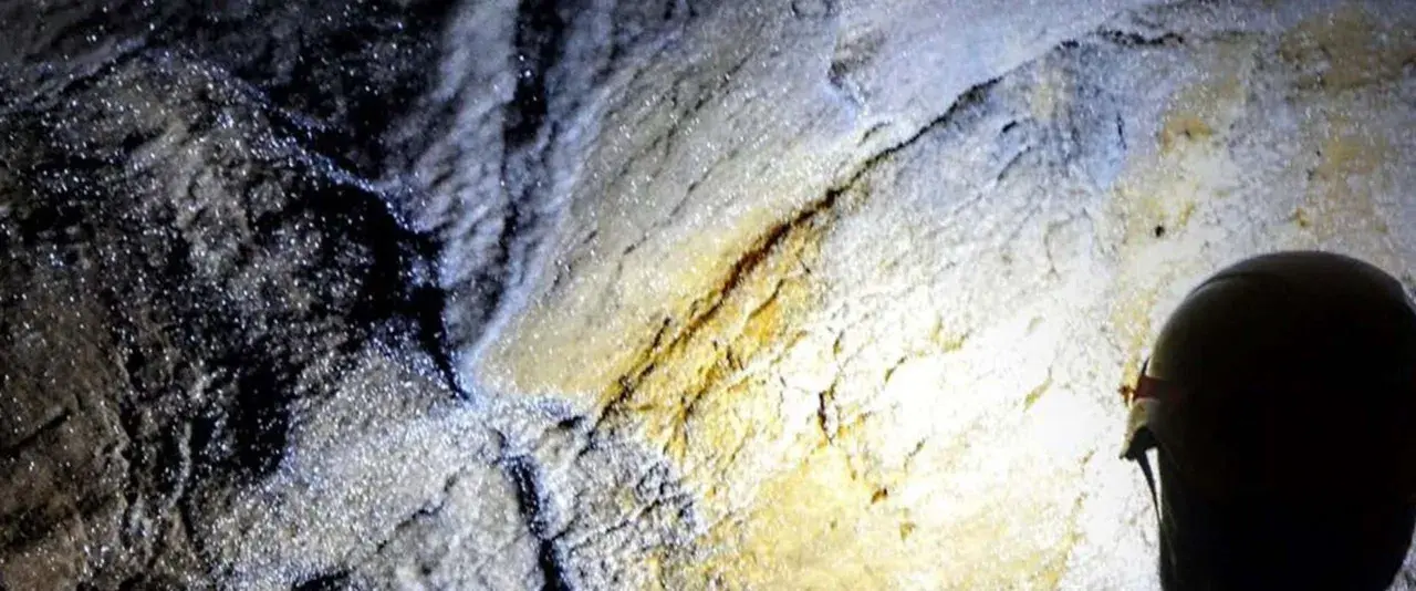 Esplorazione della grotta turistica Antro del Corchia: rocce scintillanti e un casco illuminato da una torcia.