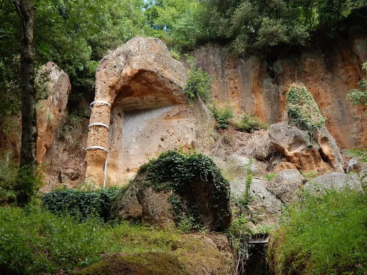 Antica tomba etrusca scavata nella roccia, con un pilastro decorato da fasce metalliche, immersa nel verde della necropoli di Sovana.