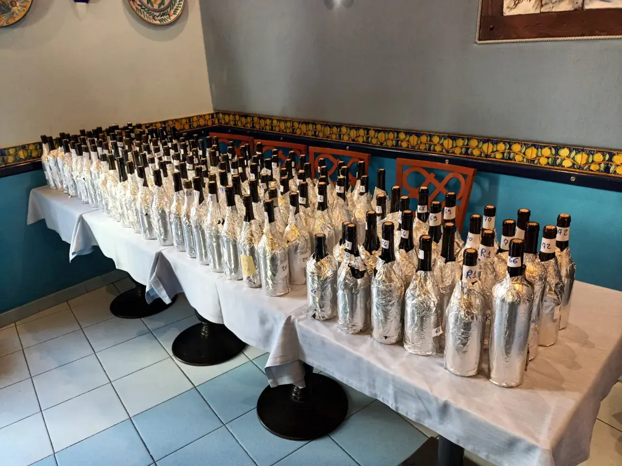 Many wine bottles wrapped in foil, lined up on a table for a tasting.