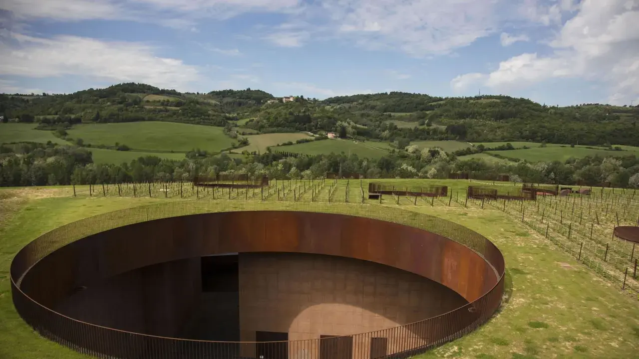 Un'avveniristica cantina toscana si fonde con il paesaggio collinare, con un tetto verde e un pozzo circolare in corten.