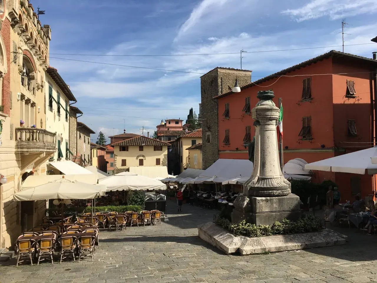 Piazza soleggiata a Montecatini Alto con tavolini all'aperto e un monumento.