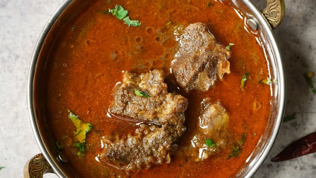 Un invitante buglione di agnello in una ciotola metallica, con pezzi di carne tenera immersi in un ricco sugo speziato e guarnito con erbe fresche.