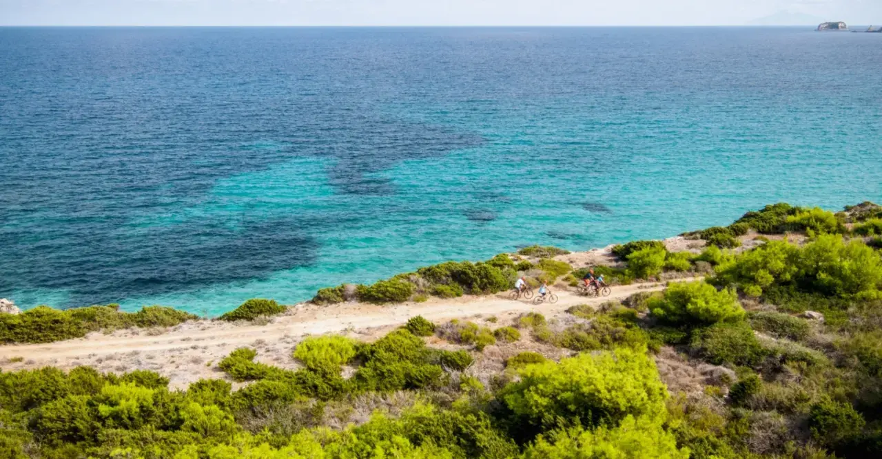 Ciclisti esplorano la costa dell'isola di Pianosa, con acque cristalline e vegetazione mediterranea.