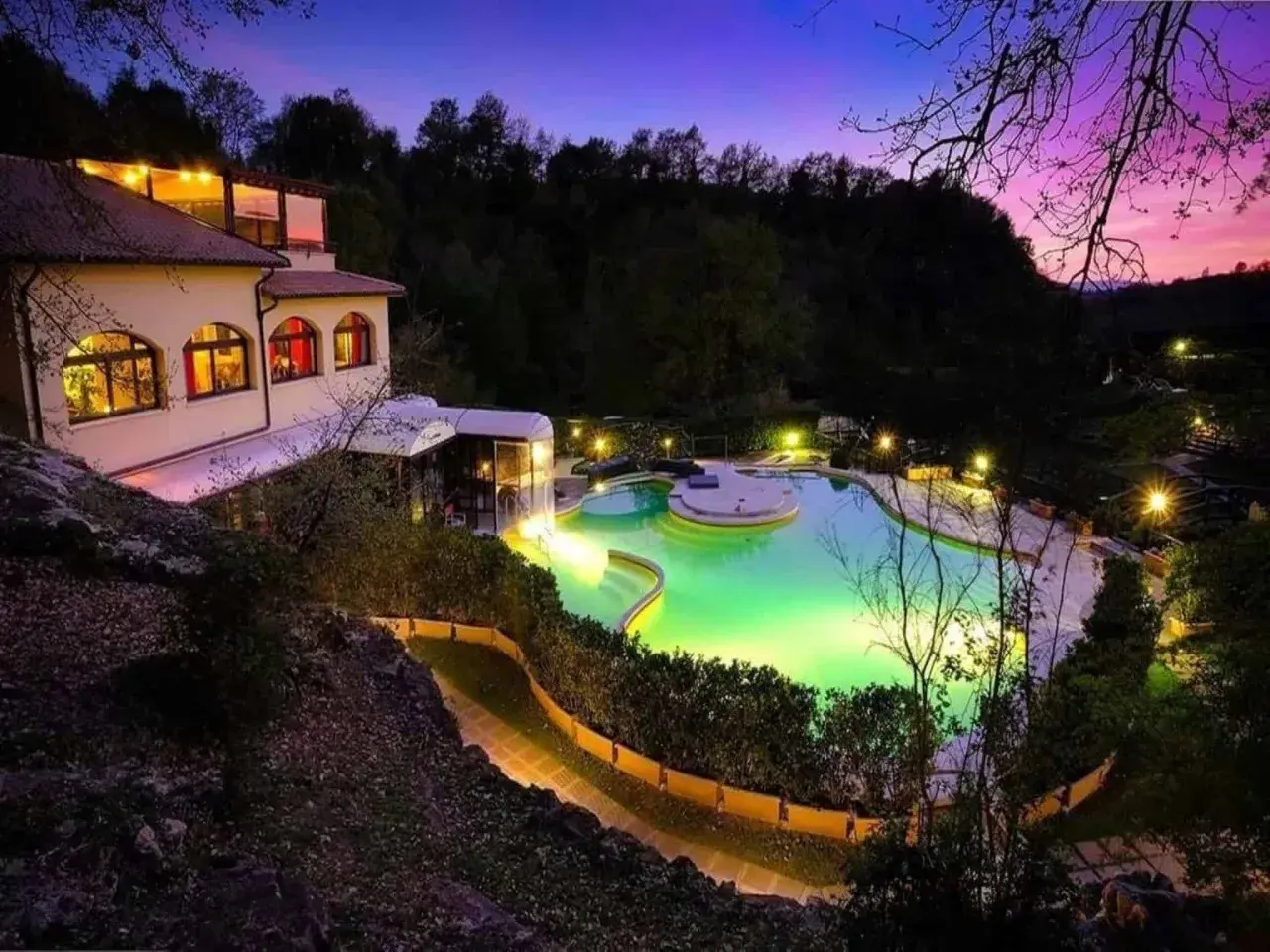Piscina illuminata e un edificio a San Carlo Terme al tramonto, con cielo viola e rosa.