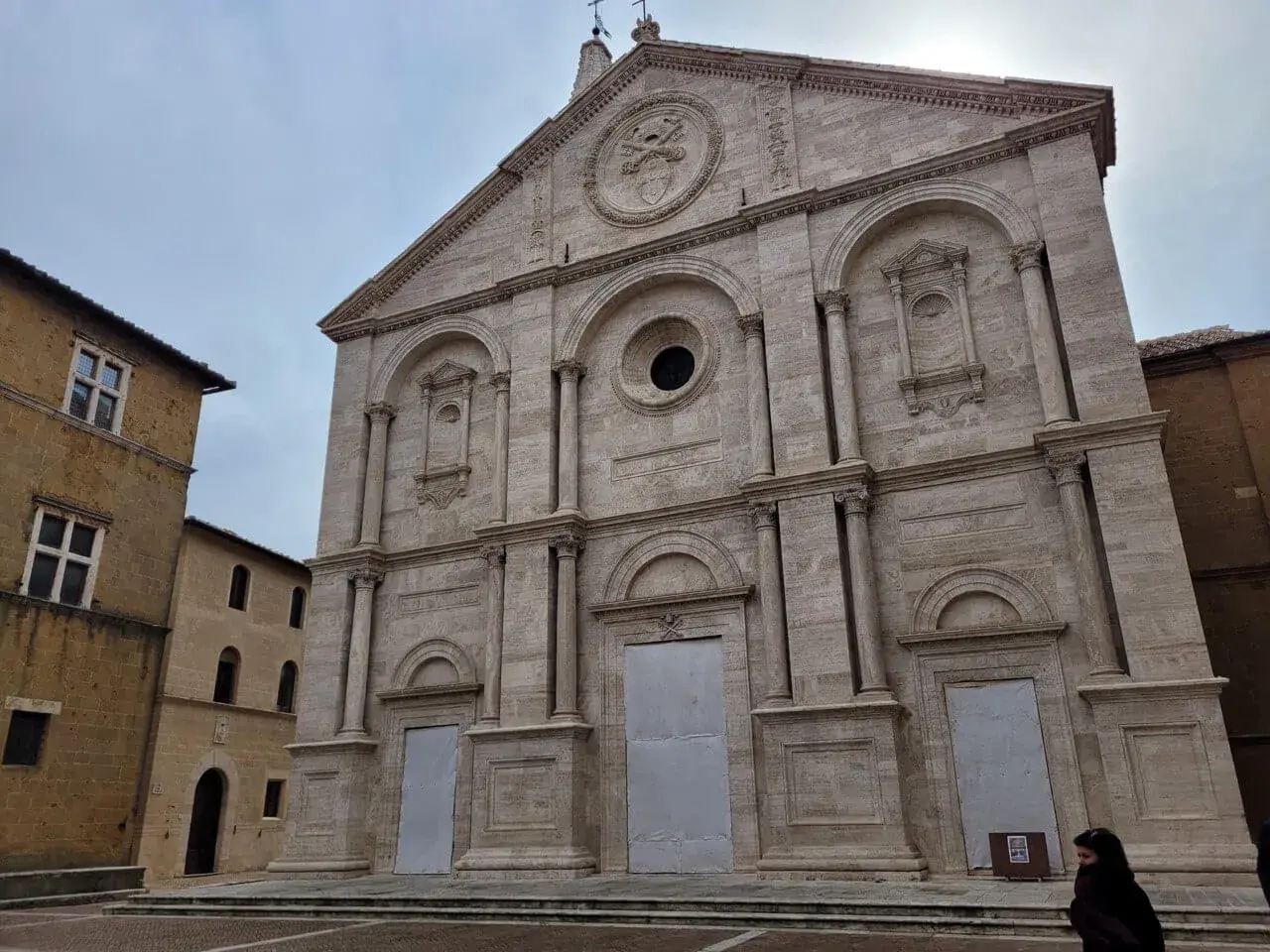 Facciata imponente del Duomo di Pienza, con accanto un edificio in pietra che ricorda il Palazzo Piccolomini.
